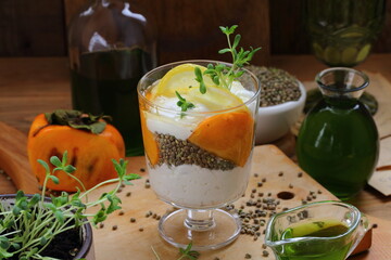 Dessert with yogurt, persimmon and hemp sativa sprouts on wooden background