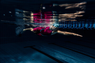 Underwater shooting. One female swimmer training at pool, indoors. Underwater view of swimming movements details.