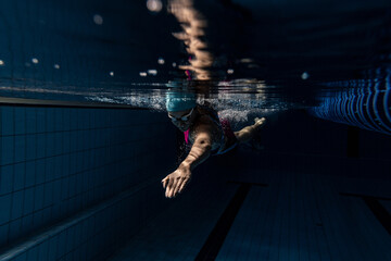 Underwater shooting. One female swimmer training at pool, indoors. Underwater view of swimming...