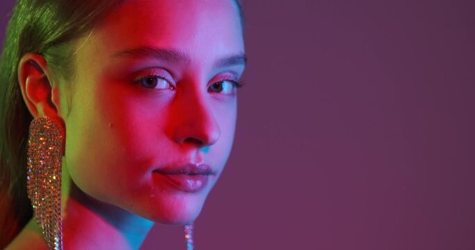 Face of sensual young woman with long earring in neon ultraviolet light