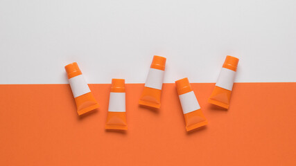 Orange tubes with white templates for names on a white and orange background. Flat lay.