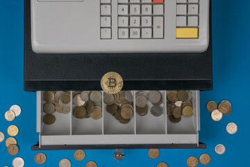 An open cash register with coins and a digital coin lying on top.