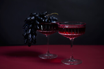 2 wine glasses, a bottle of red wine, a bunch of dark grapes. a stylish, tempting offer advertising red wine. space for copying. wine list. restaurant advertising.romantic dinner for two.