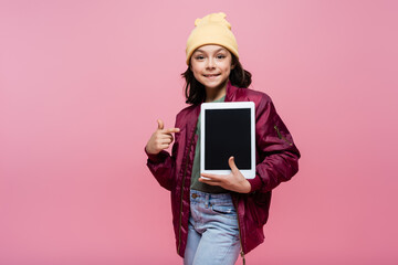 happy preteen girl in trendy outfit pointing with finger at digital tablet with blank screen...