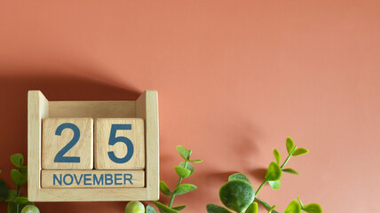 November 25, Date design with calendar cube and leaf on orange background.