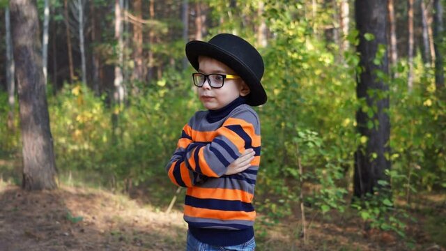 Little boy in hat and glasses makes funny grimaces standing in the park.