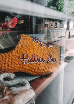 Storefront bakery window, a Dutch shoe holding pink tulips, covered in yellow cake frosting with Pella, Ia spelled out in frosting, a plate of Dutch Letters and other pastries. Pella, Iowa, USA. 