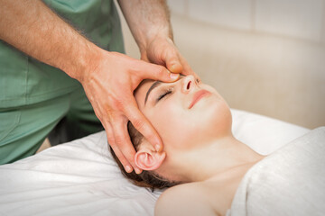 Pretty young caucasian woman receiving a head massage by a male massage therapist in a beauty salon