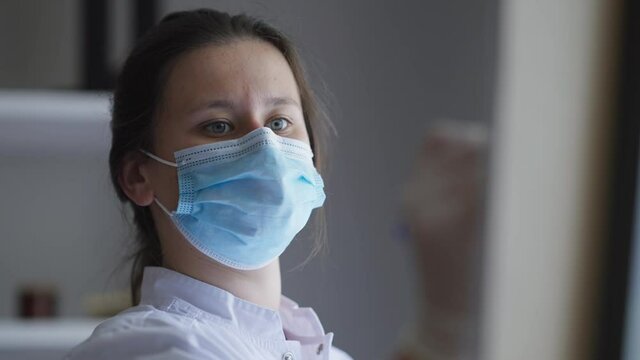 Portrait of focused woman in Covid face mask writing on flipchart thinking looking out the window. Concentrated serious female doctor scientist analyzing vax side effects and efficiency