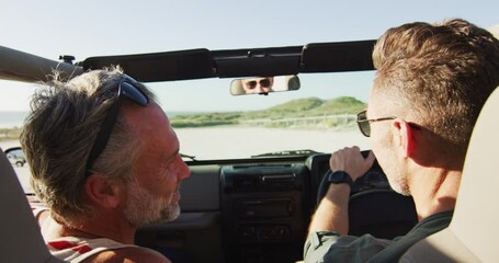 Happy caucasian gay male couple driving car and talking on sunny day at the beach