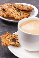 Cup of coffee with milk and fresh baked oatmeal cookies on white plate. Delicious crunchy dessert