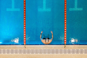 Aerial, drone top down view of professional swimmer, swimming in the swimming pool. High quality photo