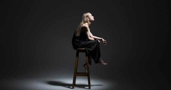 Profile of beautiful fashion model sitting on stool over black background