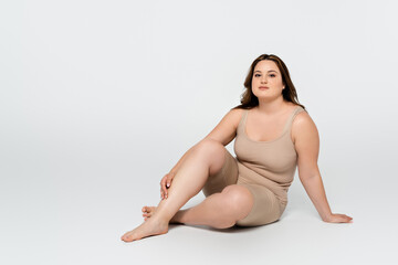 Obraz premium Young body positive woman looking at camera while sitting on grey background.