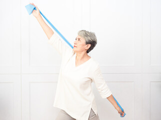 Senior asian woman doing exercises with resistance band at home.