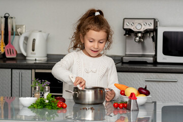 A little pretty girl cooks in the kitchen from fresh vegetables. Conceptual photography. Proper...
