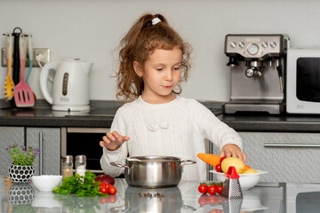 A little pretty girl cooks in the kitchen from fresh vegetables. Conceptual photography. Proper...