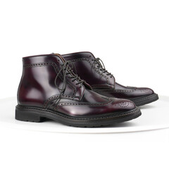 Fototapeta na wymiar Burgundy polished calfskin brogue boots with laces on white background