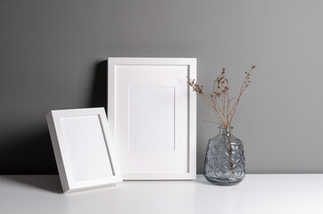 Two portrait frames mockup for artwork, photo and print presentation over grey wall with dry plant twigs decorations. Minimalist style interior.