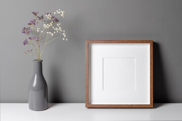 Square wooden frame mockup for artwork, photo, print and painting presentation with dry flowers over grey wall.