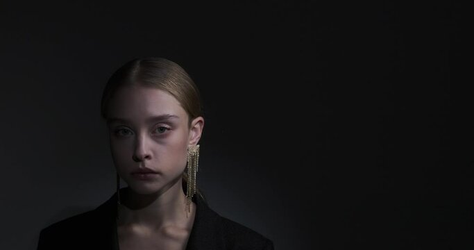 Serious female fashion model with diamond earring over black background