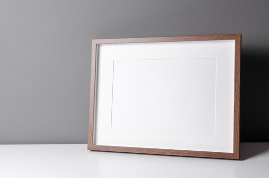 Landscape wooden frame mockup for artwork, photo and print presentation on white table over grey wall. Minimalist interior design.