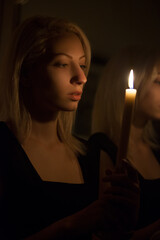 Beautiful blonde with a burning candle in the twilight.