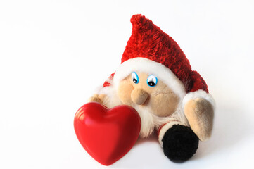 A cute gnome on a white background sits and wants to take a decorative red heart.