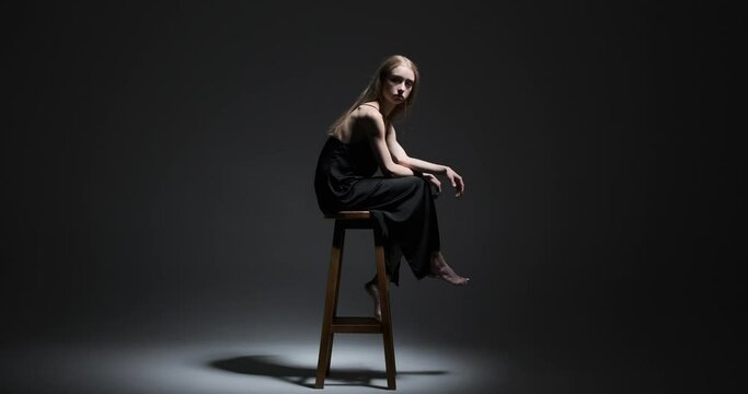 Beautiful fashion model sitting on high stool over black background