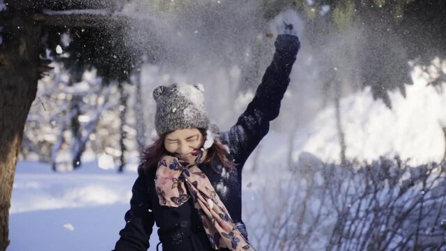 Happy young woman pulling the snowy branch of tree over her head. Winter, sport, holidays, relationship, love, xmas, lifestyle concept. Filmed on cinema camera, 10 bit color space.