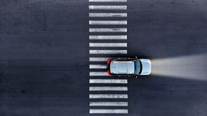 Aerial. A car with its headlights on drives over a pedestrian crosswalk at night. Top view from...