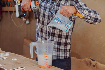 Fototapeta na wymiar Carpenter mixing epoxy resin with an electric mixer in liquid cup in workshop