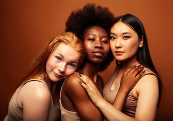 young pretty asian, caucasian, afro woman posing cheerful together on brown background, lifestyle diverse nationality people concept