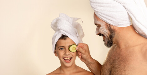 Father and son special facial spa day. Smiling and united family. Child with towel on head looks at...