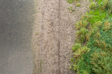 Top down view on a river and a river bank. Wet dirt, small stones and green grass is visible. The water is clear and stones underwater create a natural background. Abstract transition in the nature.