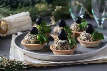 Holiday snack in tartlets with mushrooms, egg and black olives on a gray background