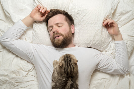 Man in white pajamas is asleep, and his adorable cat lies on his chest. Top view. 