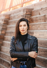 A young brunette woman in a black leather jacket in the park in the fall. Walking to the city street.