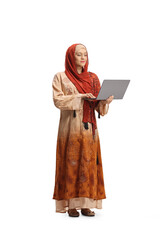 Full length portrait of a woman wearing a hijab, standing and orking on a laptop computer