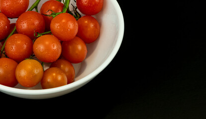Branch of ripe cherry tomatoes on plate, top view in the black background. Close up photo