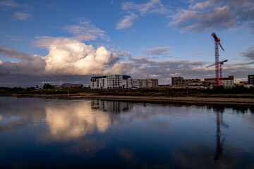 Naklejka premium Cloud over construction site Kade Zuid part of the new Noorderhaven neighbourhood reflecting in river IJssel in Zutphen. Aerial industrial view of building plot. Housing and urban management.