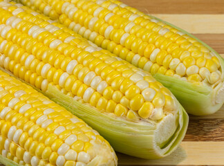Fresh corn on cobs on wooden table, closeup. Sweet corns on wooden board.