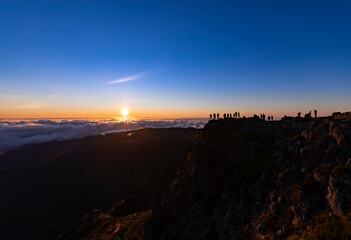 Fototapeta na wymiar Colorful sunrise panorama on the mountain top of “Pico do Arieiro“ on Madeira island Portugal. Silhouettes of people on a viewing platform taking pictures and enjoying october dawn in early morning