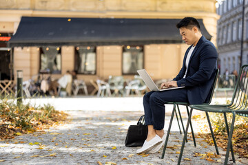 Focused asian businessman typing on laptop during work outdoors. Concept of remote work and...