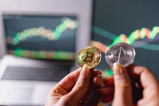 close-up crypto coins. Unrecognizable female hand holds an ethereum and a bitcoin coin with computers representing trend and graphics on background.