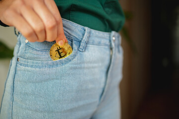 Unrecognizable female puts a golden bitcoin coin inside of her jeans pocket. Crypto currency and trading business concept. To invest savings in virtual money.