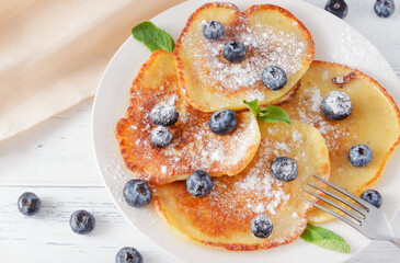 pancakes with blueberries, powdered sugar and mint on a plate, beige napkin on a white  top view
