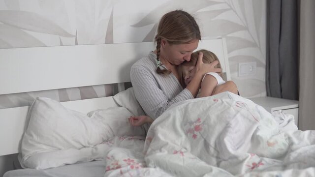 Mom presses her daughter of five years to her chest and gently strokes her head in the morning in bed.