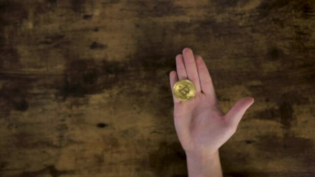 Top view unrecognizable cropped male hand tossing a golden bitcoin coin.