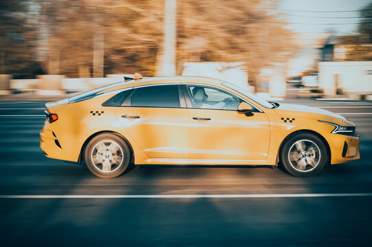 Orange car Kia K5 Fifth generation DL3 speed driving on asphalt city road with autumn blurred background. City taxi car with checkers on roof in fast motion